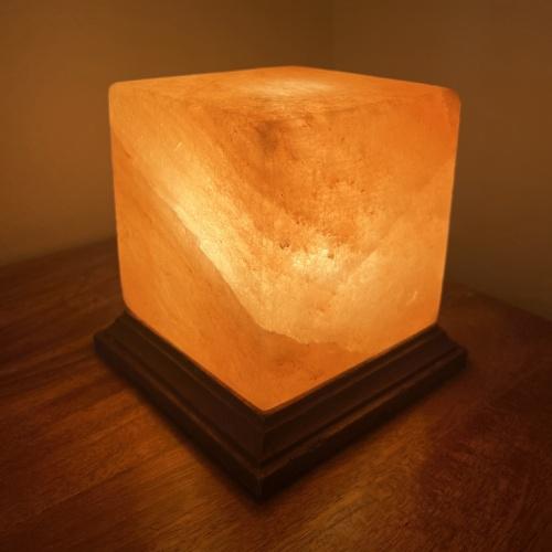 Ljus saltstenlampa på mörkt träunderlag.