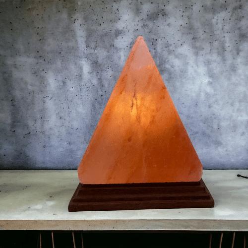 Orange, trekantig saltlampa på träfot.