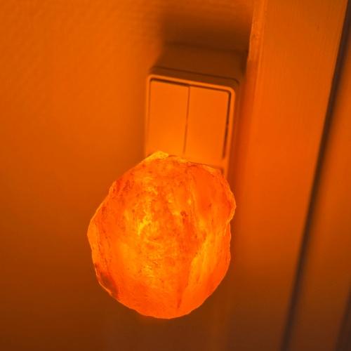 Ljusorange bergsaltlampa tänd, väggmonterad.